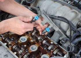 Car mechanic fixing fuel injector at two camshaft gasoline engine